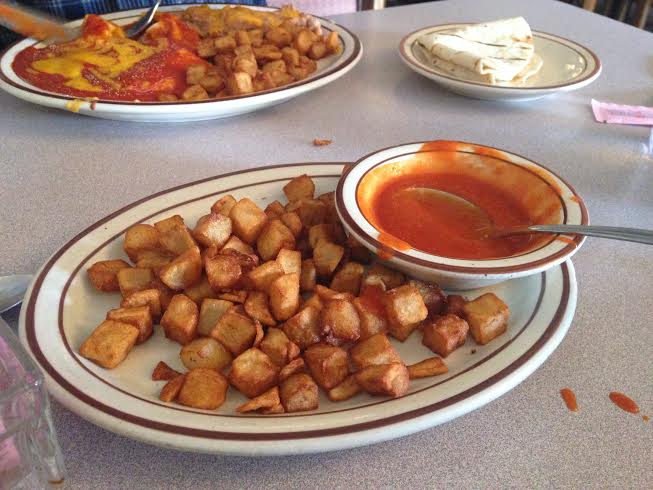 Side of potatoes and red chili, with juevos rancheros in the background